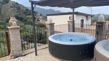 A hot tub on a rooftop terrace with a view of a mountainous landscape.