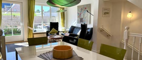 A modern living room with a dining table, chairs, a sofa, and a large window with curtains.