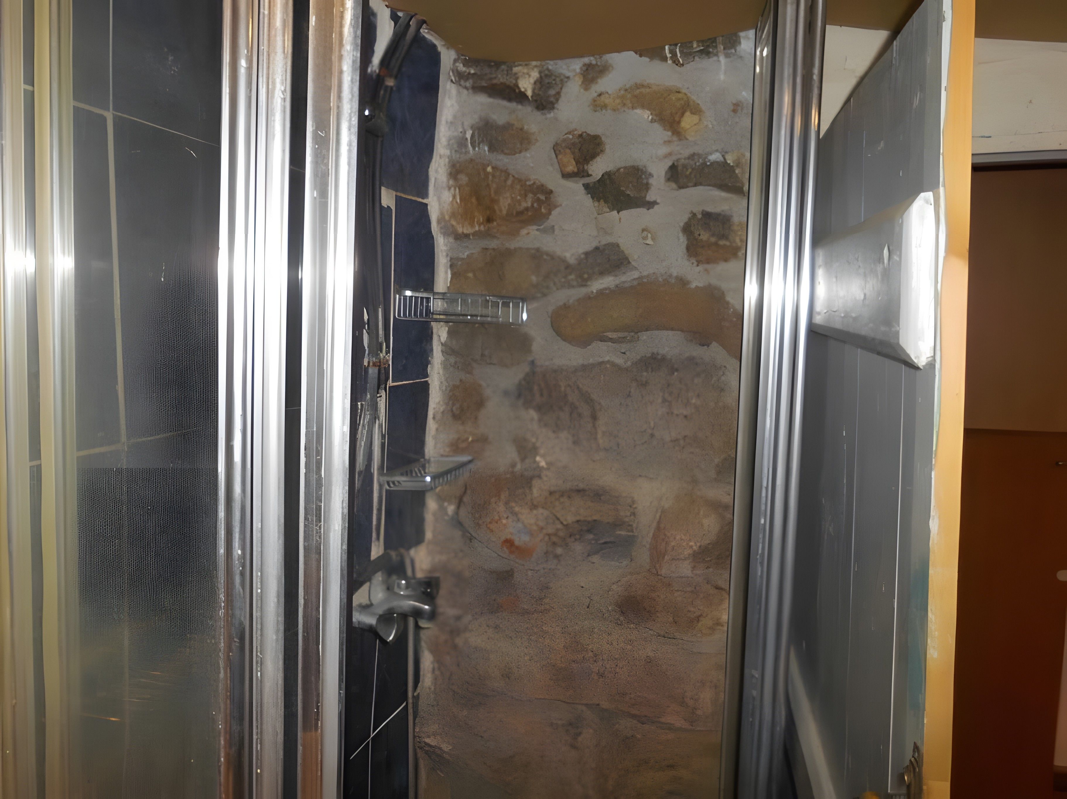 Un vano con pared de piedra y marco de puerta metálico.