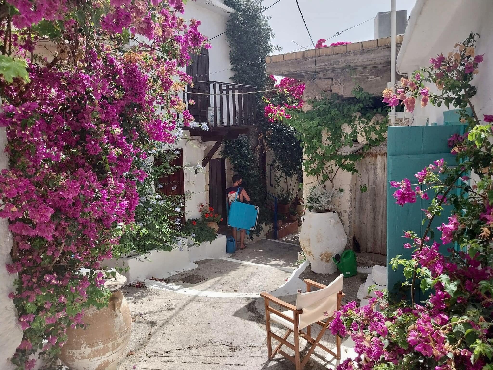 Un estrecho callejón con un edificio blanco, un balcón y flores de buganvilla.