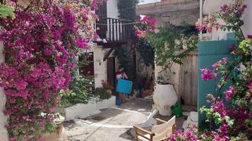 Un estrecho callejón con un edificio blanco, un balcón y flores de buganvilla.