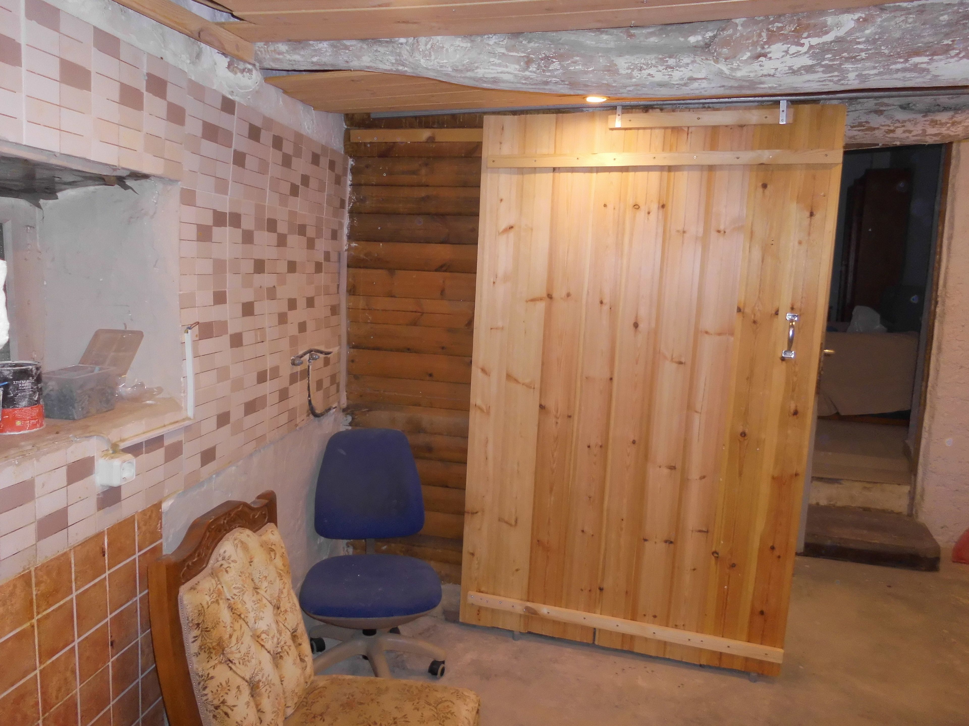 Ein Zimmer mit Holztür, blauem Bürostuhl, gemustertem Sessel und einer Wand mit Fliesen.