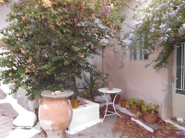 Un patio con una mesa blanca, una maceta de terracota grande y plantas en macetas.