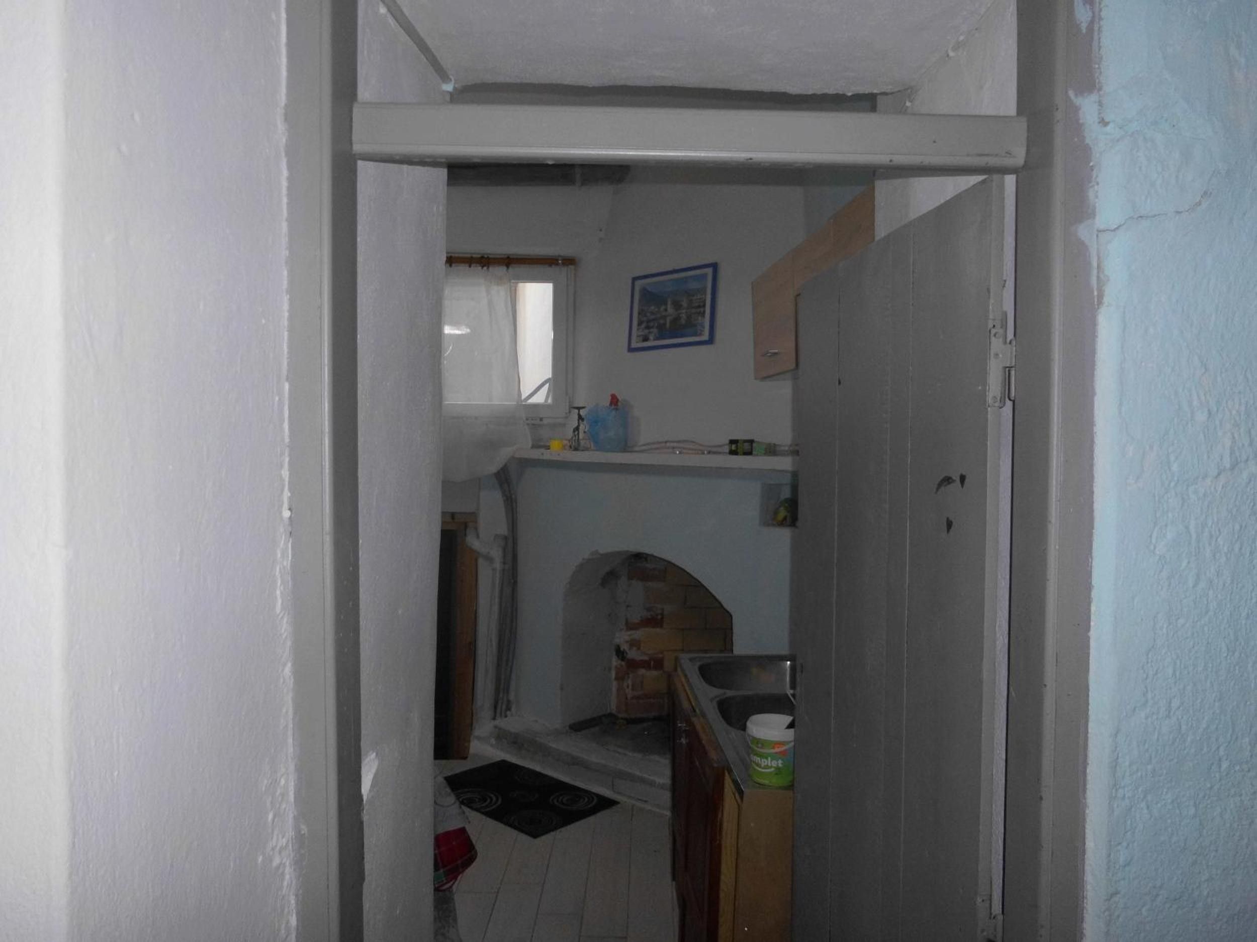 Un pasillo estrecho que conduce a una zona de cocina con un lavamanos, una ventana y una puerta.