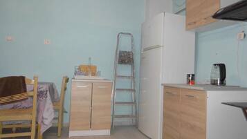 Una cocina funcional con armarios de madera, un refrigerador blanco, una mesa con mantel y una tetera en la encimera.