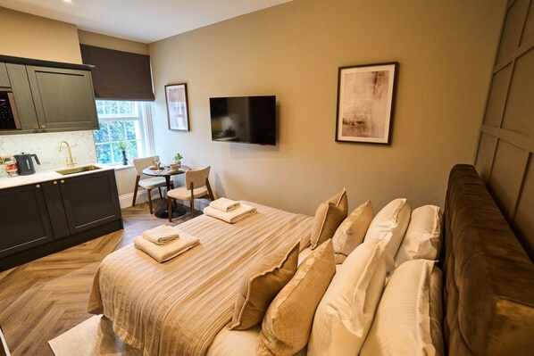 A hotel room with a bed, a desk, a chair, a TV, and a kitchenette. - *NEW* Peaceful Suite With Orchard Views, Near Goodwood (Warningcamp)