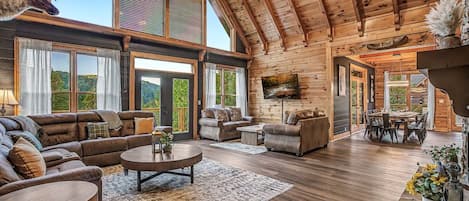 A spacious living area with a high ceiling, large windows, and a fireplace.