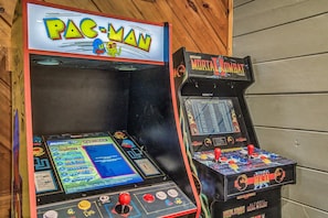 Zwei Spielautomaten, einer mit der Aufschrift 'PAC-MAN' und der andere mit 'Mortal Kombat', mit Joysticks und farbenfrohen Bildschirmen.