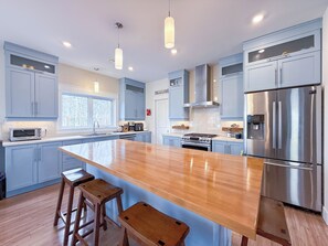 A modern kitchen with a central island, stainless steel appliances, and light blue cabinetry. - Unit A/ Spacious/ Heated pool/ Close to beach/ On-site Activities! (Brackley Beach)