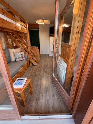 Una escalera de madera conduce a una zona de dormir en un altillo con un sofá y una pequeña mesa.