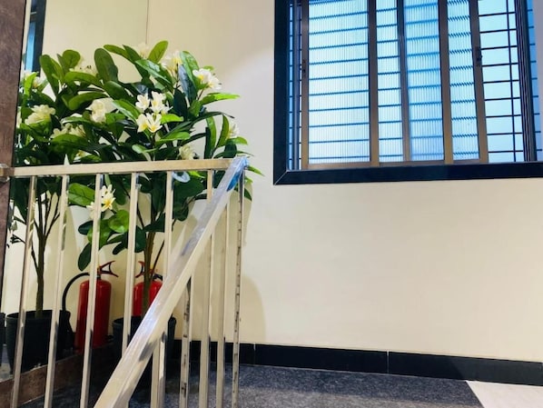 A staircase with a railing, potted plants, and a window with blinds. - Hotel Rox Inn (Mumbai)