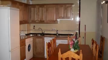 A compact kitchen with wooden cabinets, a built-in dishwasher, and a dining table with chairs.