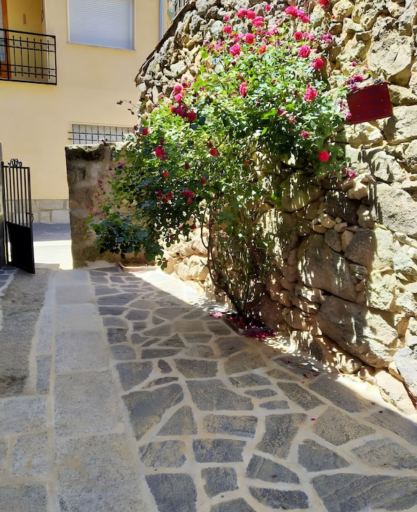 A stone pathway leading to a building with a stone wall covered in pink flowers. - Country House 'Casa Rural La Cancha II' (Navalacruz)