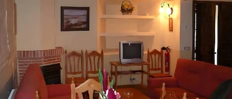 A living room with a fireplace, a television on a stand, and a dining area with chairs and a table.