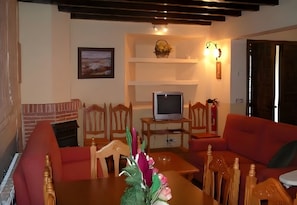 A living room with a fireplace, a television on a stand, and a dining area with chairs and a table. - Country House 'Casa Rural La Cancha II' (Navalacruz)