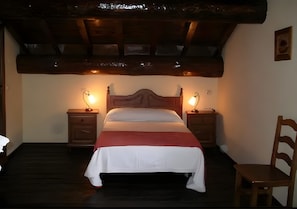 A bedroom with a wooden bed, two bedside tables, a chair, and a sloped ceiling. - Country House 'Casa Rural La Cancha II' (Navalacruz)