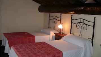 Une chambre avec deux lits simples, une tête de lit en bois, une table de chevet avec une lampe et une couvre-lit rouge à motifs.