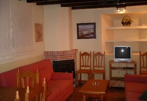 A living room with a red sofa, wooden chairs, a fireplace, a television on a wooden stand, and a framed picture on the wall. - Country House 'Casa Rural La Cancha II' (Navalacruz)
