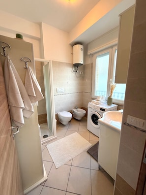 Een kleine badkamer met douche, toilet, bidet en wasmachine.