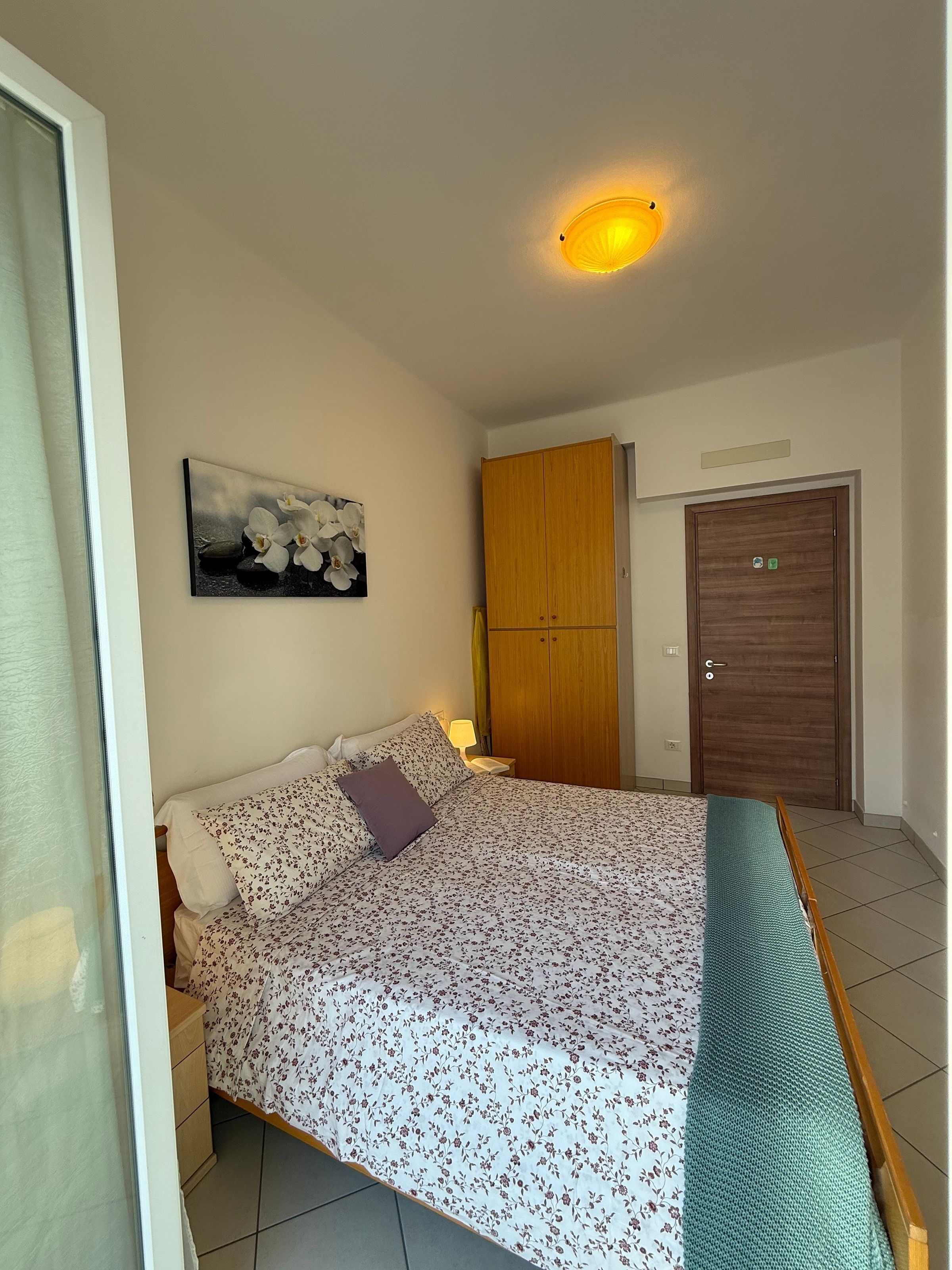 Une chambre à coucher avec un lit, une armoire en bois, une porte portant un panneau indiquant la sortie de secours et un tableau accroché au mur.