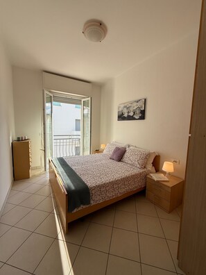 Een slaapkamer met een bed, nachtkastje, lamp, raam met uitzicht en een plafondlamp.