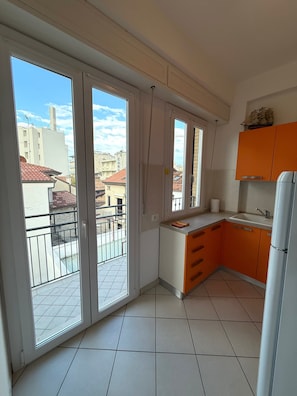 Una cocina con balcón, armarios blancos y vista a edificios.
