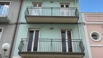 A multi-story residential building with balconies, a visible door, and a car parked in front.