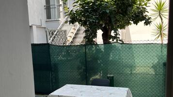 A patio with a table and chairs, a green fence, and a tree.