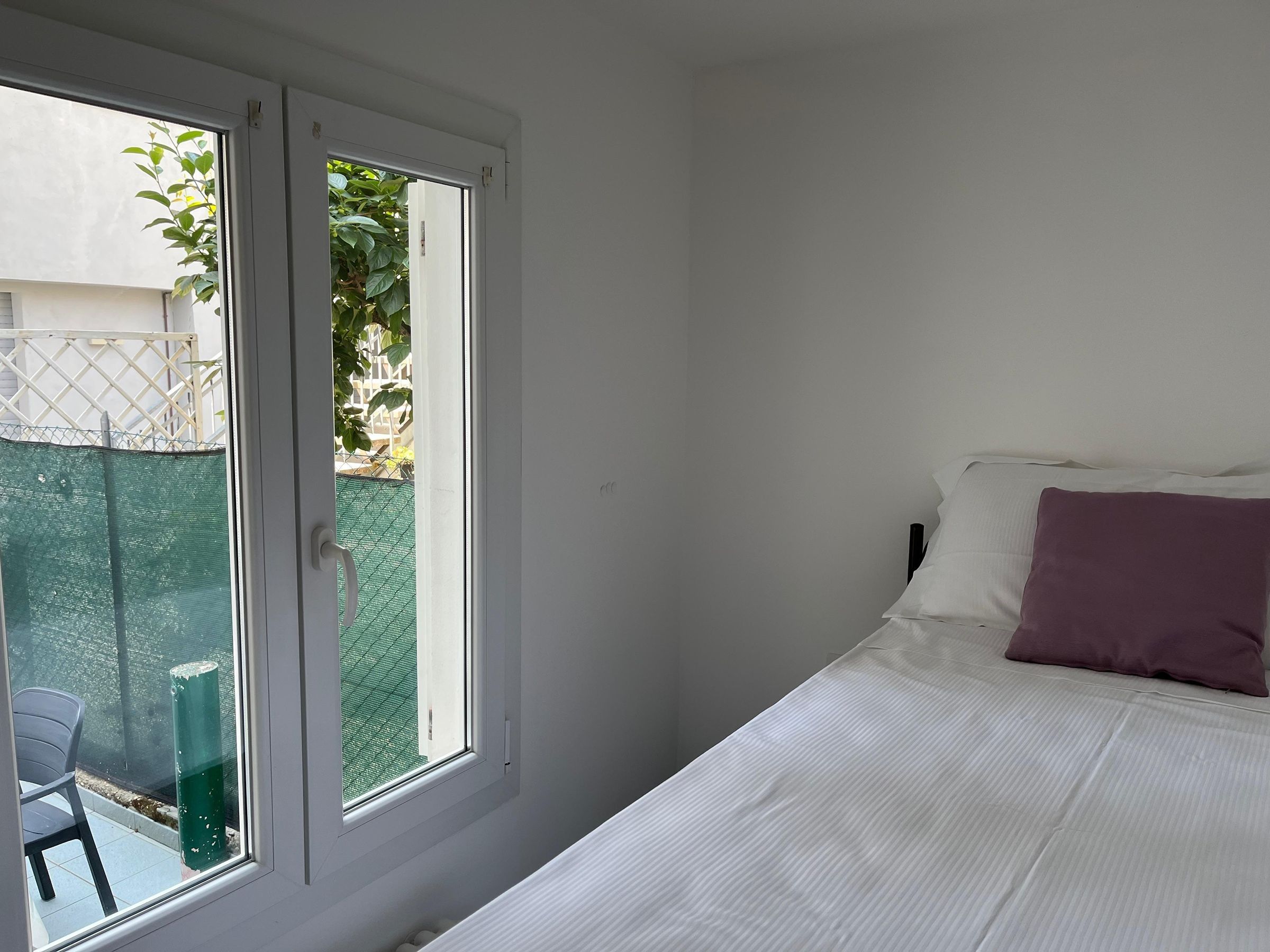 A bedroom with a bed, a window, and a view of a fenced outdoor area.