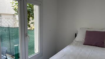 A bedroom with a bed, a window, and a view of a fenced outdoor area.