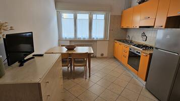 A compact kitchen with a dining table, chairs, a stove, and a refrigerator.