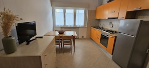 A compact kitchen with a dining table, chairs, a stove, and a refrigerator. - Apartment 'Rosa Appartamenti Pellico' with spacious ground floor and outdoor area (Cattolica)
