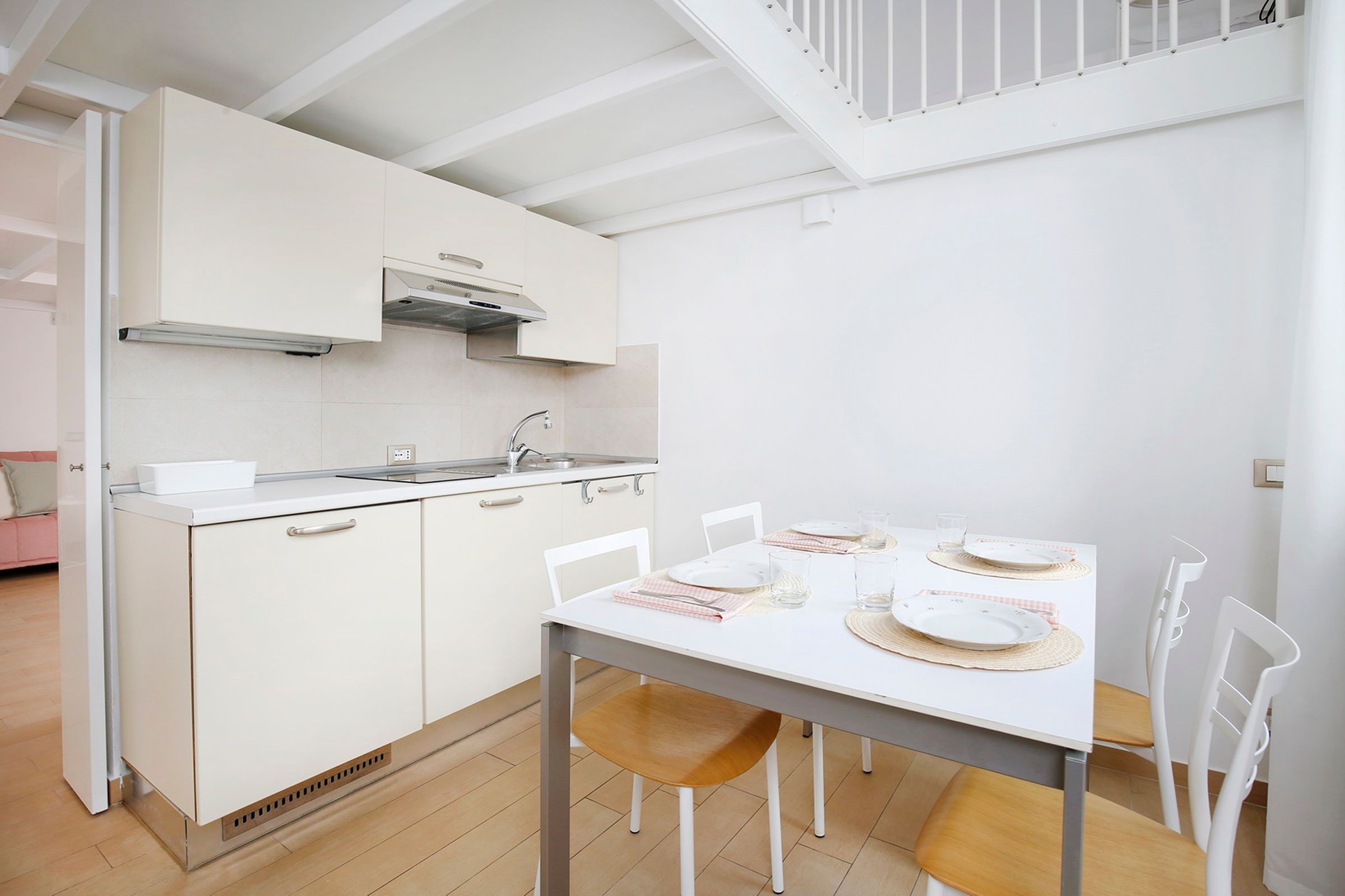 Una cucina compatta con zona pranzo, mobili bianchi e un tavolo piccolo apparecchiato per quattro persone.