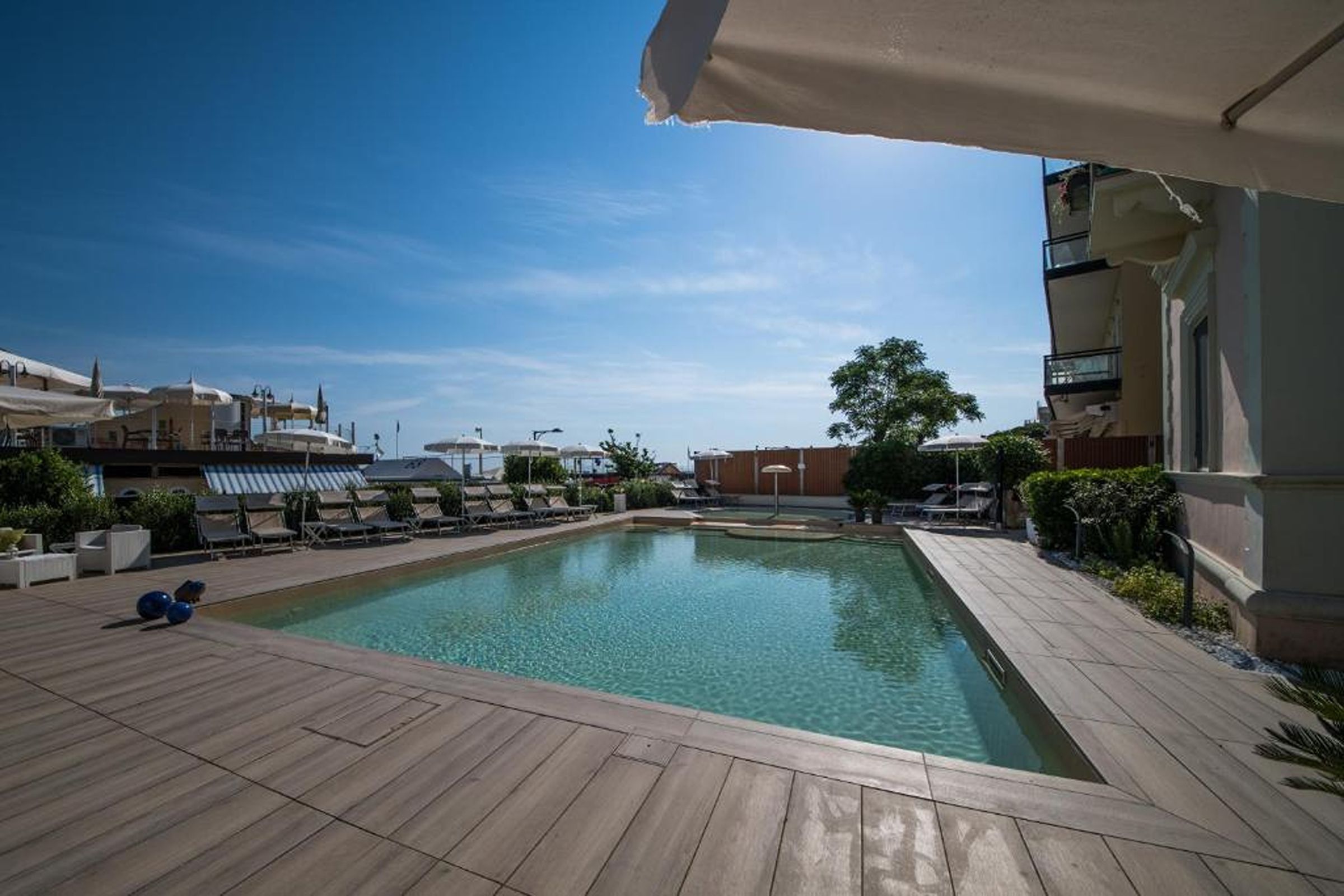 A swimming pool with lounge chairs and umbrellas, surrounded by buildings and greenery.