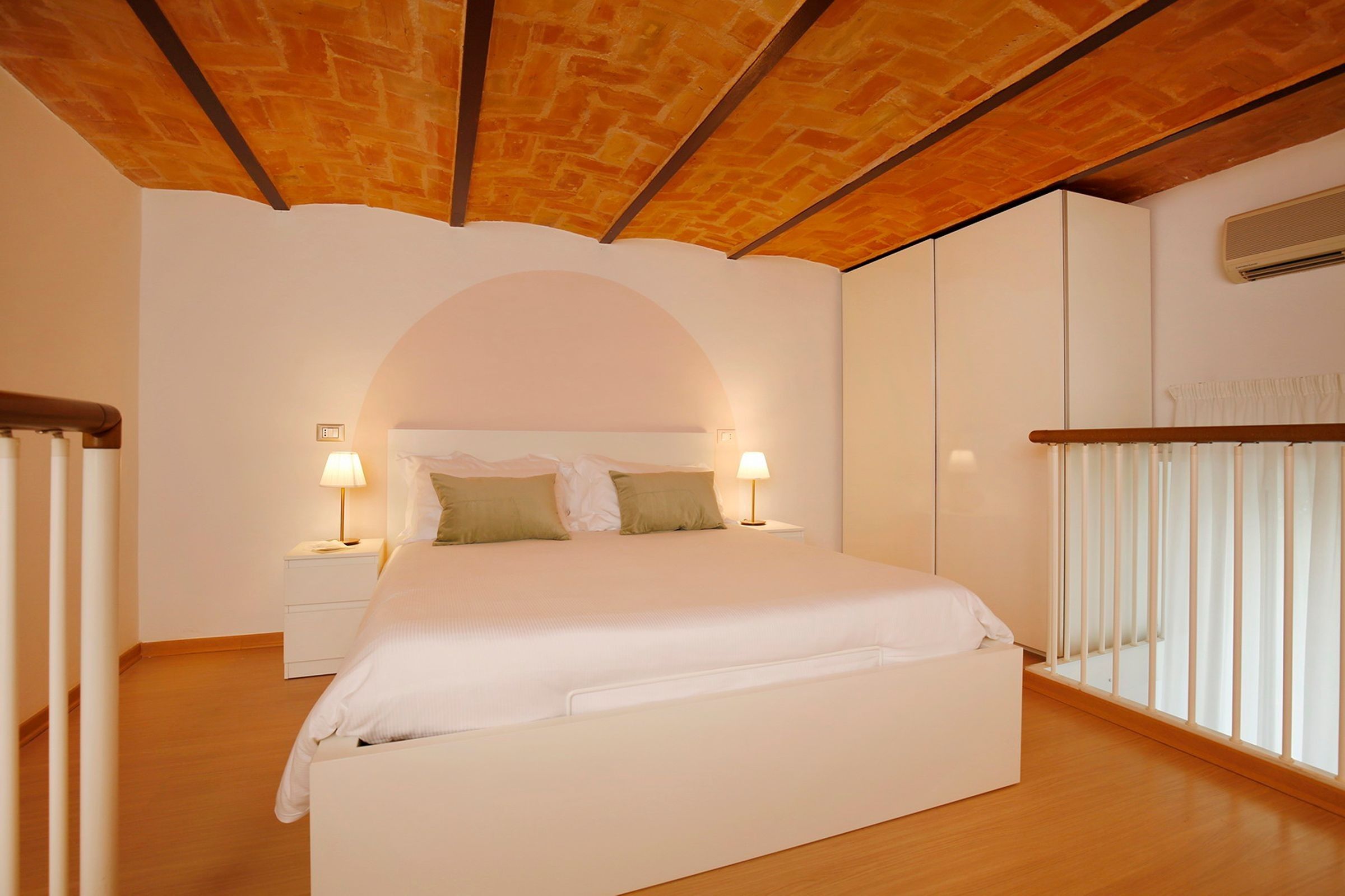 A bedroom with a wooden ceiling, a bed with white bedding, two bedside lamps, and a window with blinds.