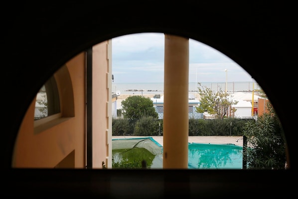 Vista a través de una ventana, con una piscina y una playa al fondo.