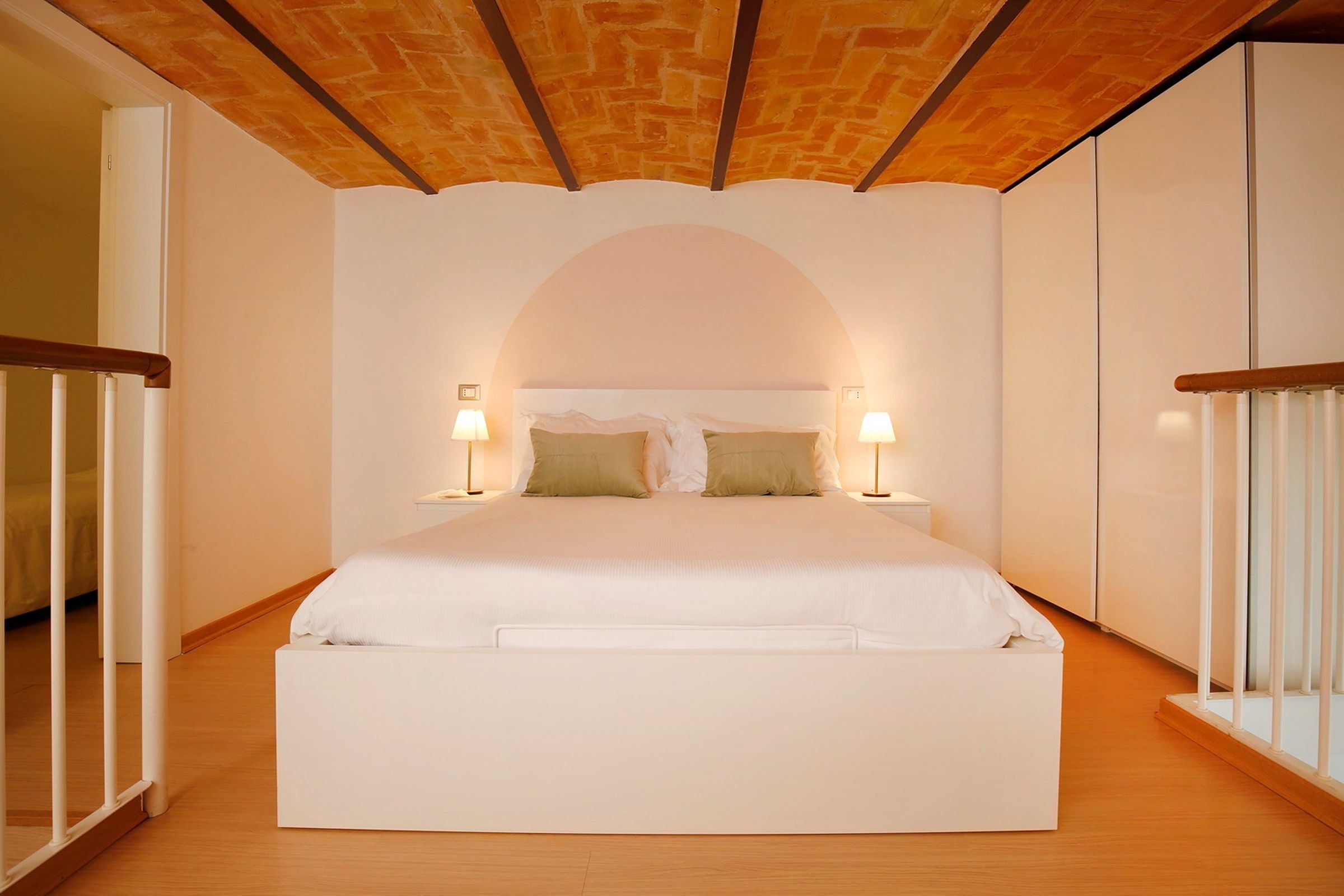 A bedroom with a large bed, two bedside lamps, and a wooden ceiling.