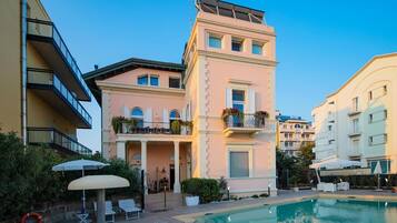 Un edificio con piscina, balconi fioriti e cielo sereno.