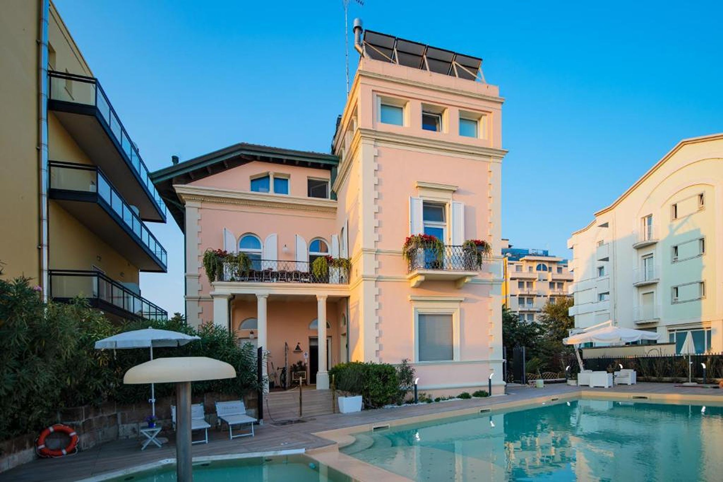 Un edificio con piscina, balconi fioriti e cielo sereno.