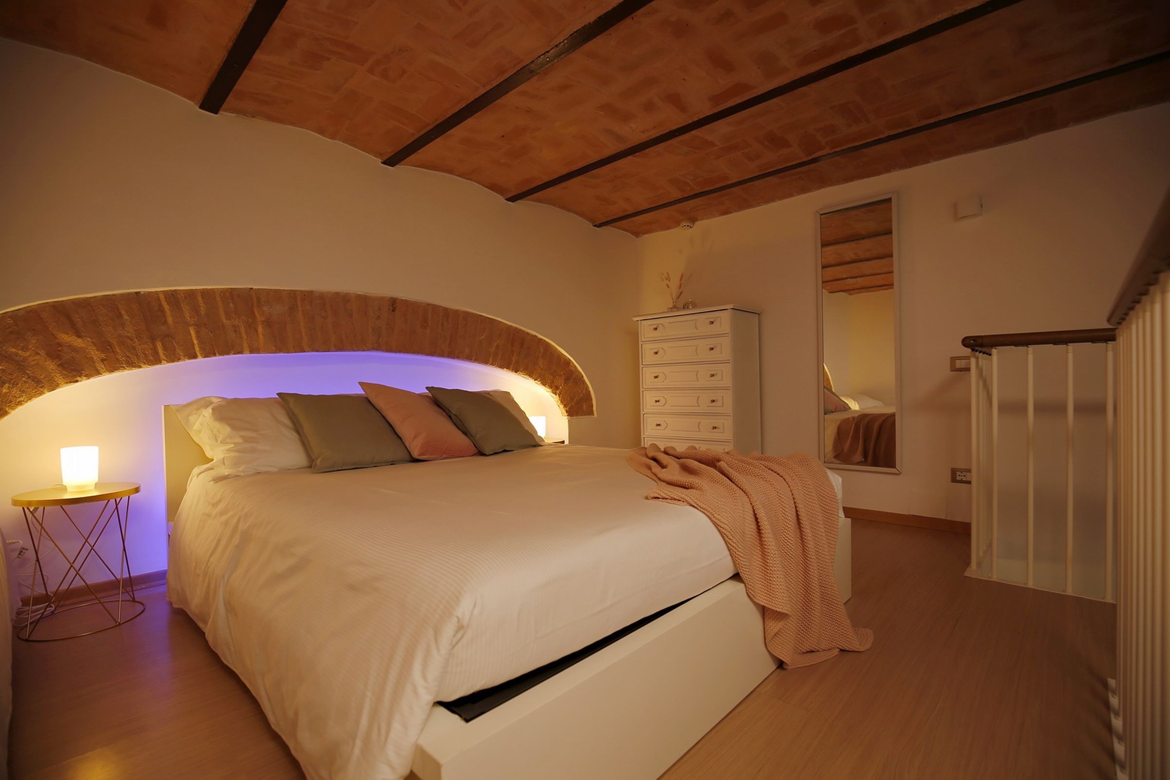 Une chambre à coucher avec un lit, une commode, un miroir et une petite table avec une lampe.
