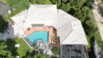 An aerial view of a house with a swimming pool, a covered patio, and a well-maintained garden.