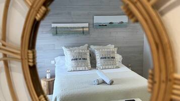 A bedroom with a bed, pillows, a bedside table, and a mirror.
