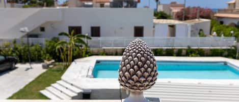 A pool with a decorative object in the foreground, a white building in the background, and a clear sky.