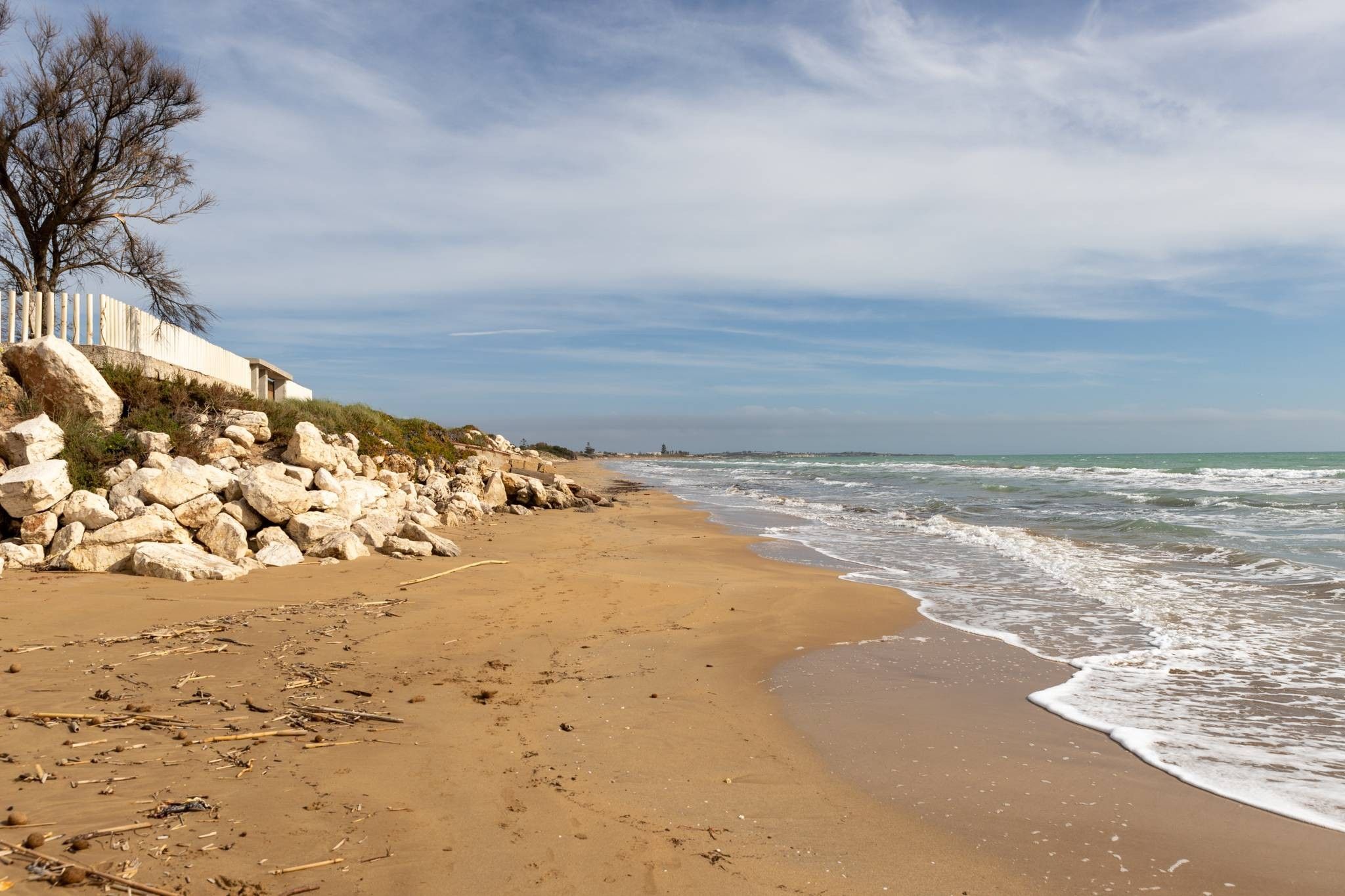 A sandy beach with a rocky cliff and a white building on the left.