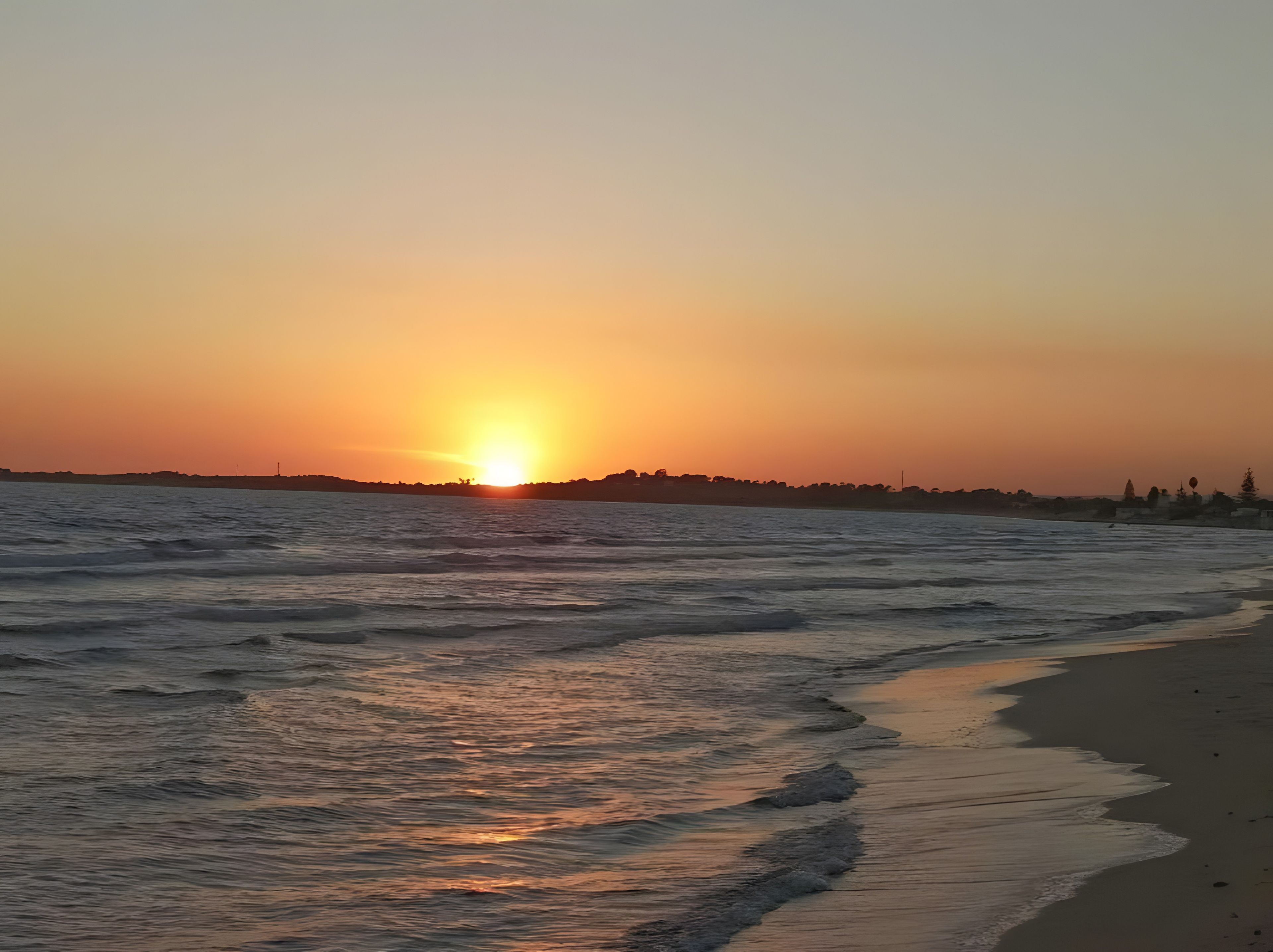 A sunset over a beach with waves gently lapping onto the shore.