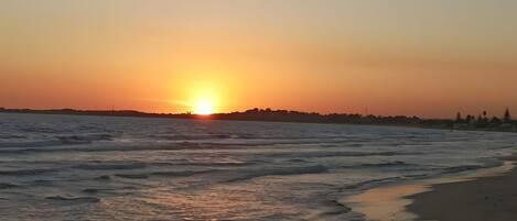 A sunset over a beach with waves gently lapping onto the shore.