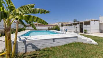 Una piscina amb una terrassa de fusta, una escala i una palmera al primer pla.