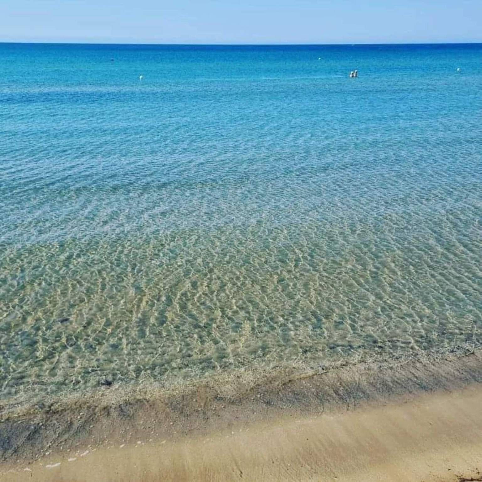 Ein Strand mit klarem, flachen Wasser und einem sandigen Ufer.