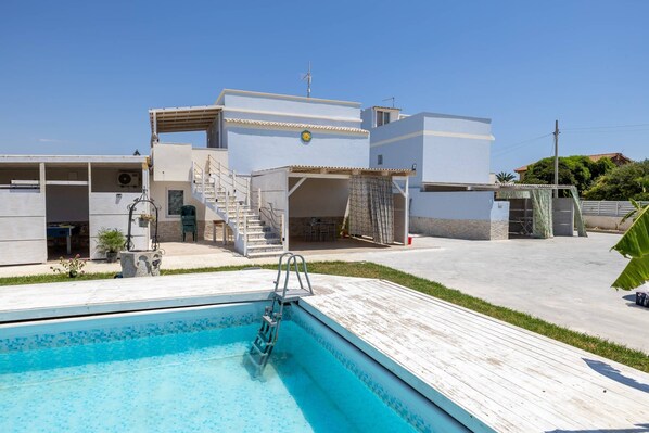 A modern building with a swimming pool, outdoor seating, and a covered patio area. - Apartment 'Stella Marina' with Shared Pool, Wi-Fi and Air Conditioning (Granelli)