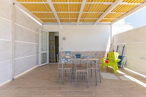 An outdoor patio with a table and chairs, a yellow chair, and a door with patterned curtains. - Apartment 'Stella Marina' with Shared Pool, Wi-Fi and Air Conditioning (Granelli)
